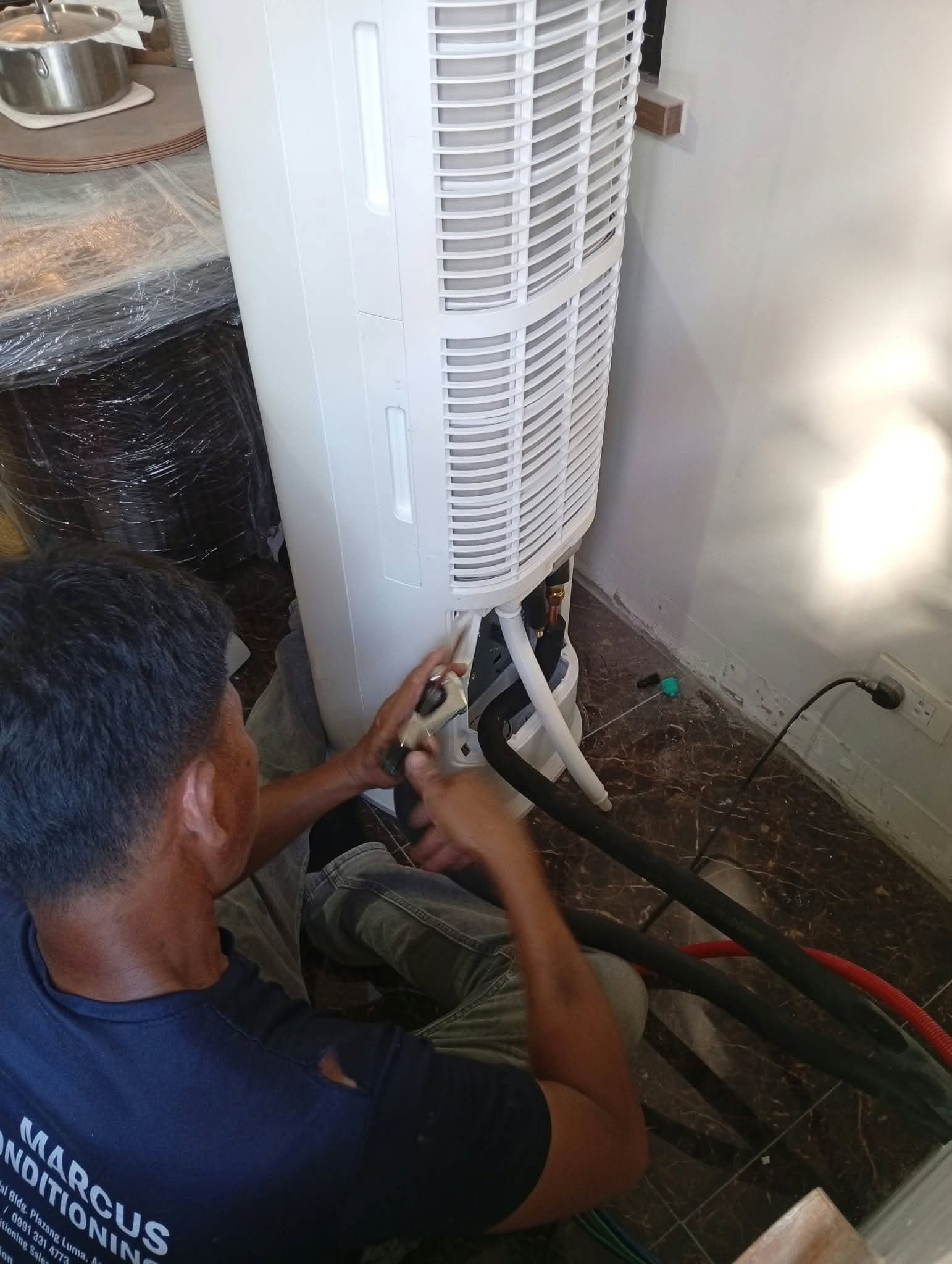 A Marcus technician connecting the pipework at the base of a floor-standing aircon unit